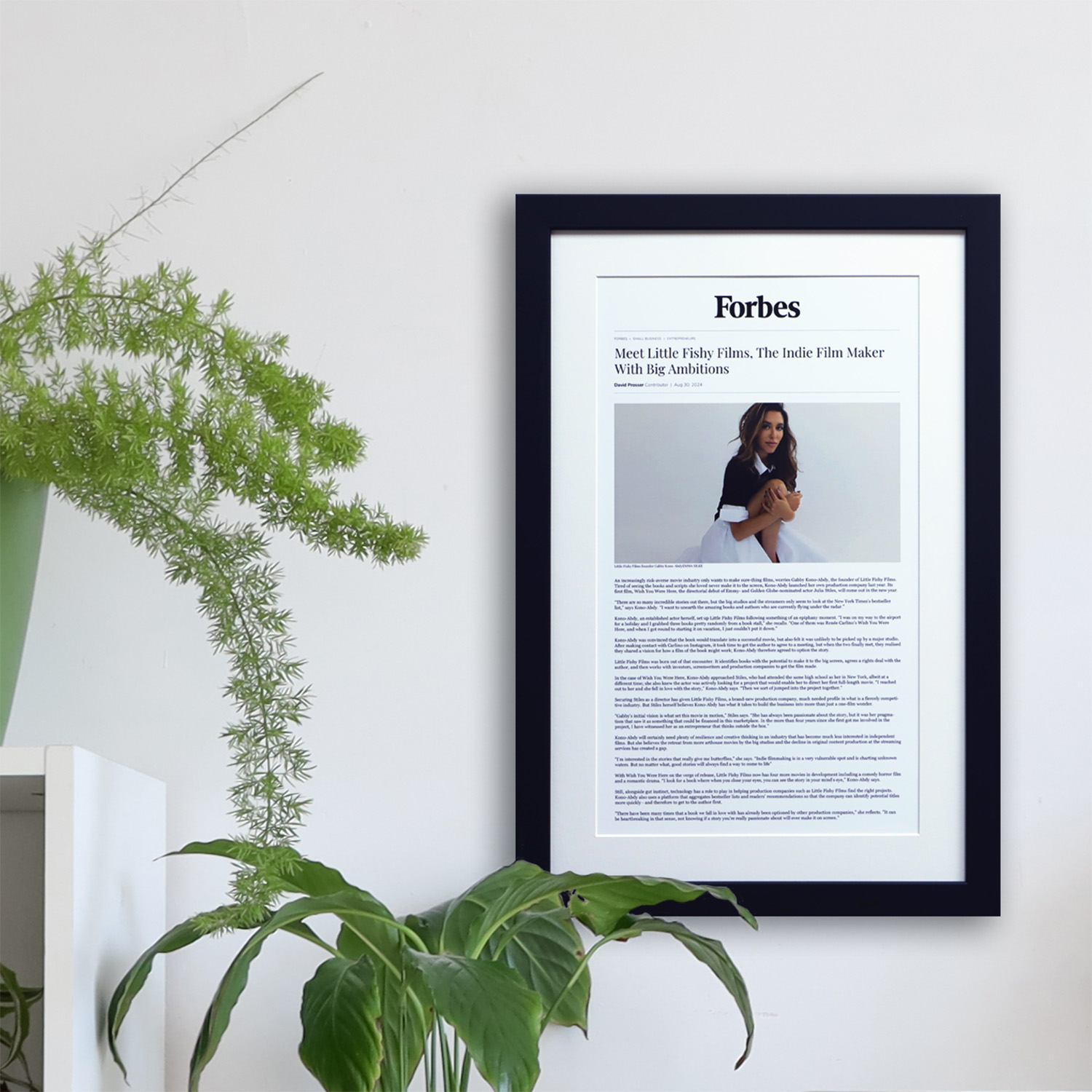 Custom framed online article wall decor above a modern desk with indoor plants, styled home office inspiration.