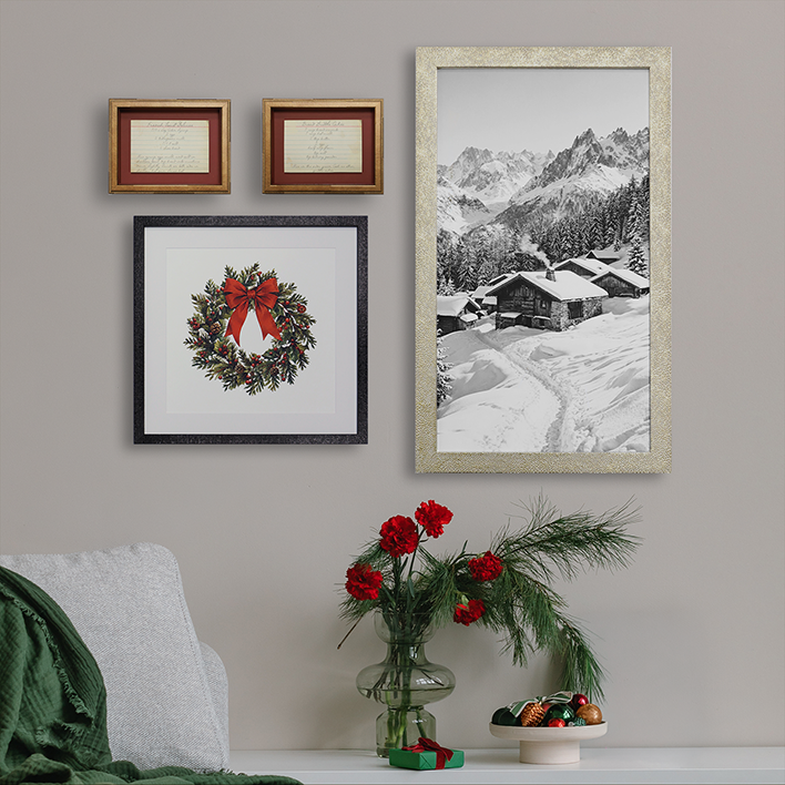 Curated holiday gallery wall above a sofa featuring framed winter cabin photography, a Christmas wreath print, and vintage handwritten notes in coordinating frames.